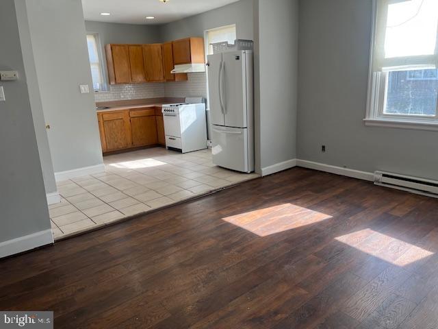 kitchen with tasteful backsplash, a baseboard radiator, white appliances, and light hardwood / wood-style flooring