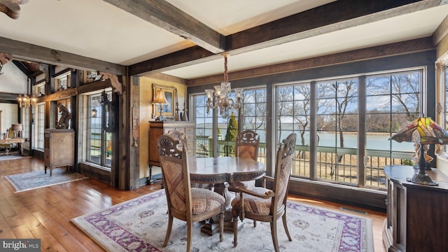 dining space with a water view, wood finished floors, visible vents, beam ceiling, and an inviting chandelier