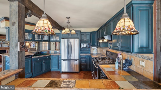 kitchen featuring blue cabinets, appliances with stainless steel finishes, hanging light fixtures, and under cabinet range hood