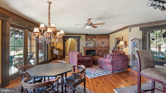 dining area featuring ceiling fan with notable chandelier, a glass covered fireplace, stairway, and wood finished floors