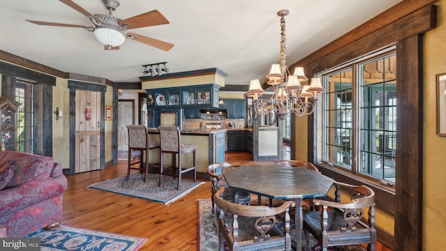 dining space with ceiling fan with notable chandelier, wood finished floors, and rail lighting