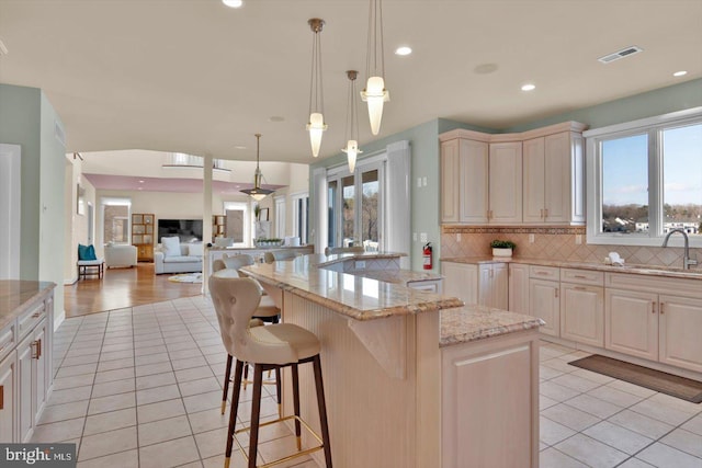 kitchen featuring pendant lighting, sink, a center island, light tile patterned floors, and light stone countertops