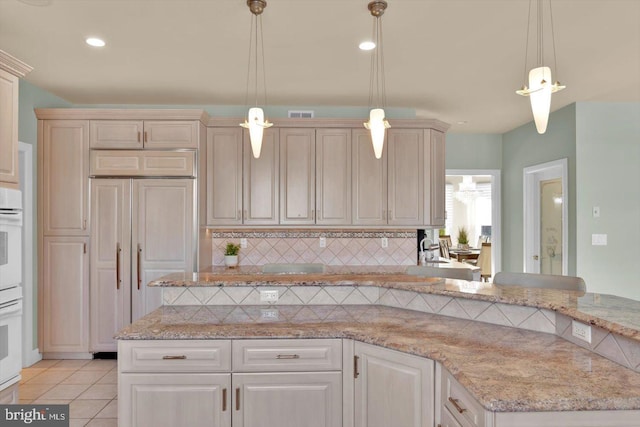 kitchen featuring hanging light fixtures, light tile patterned floors, cream cabinetry, light stone countertops, and backsplash