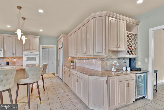 kitchen with light tile patterned flooring, pendant lighting, sink, wine cooler, and light stone countertops