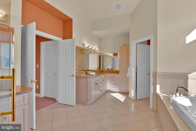 bathroom featuring a relaxing tiled tub, vanity, and tile patterned flooring