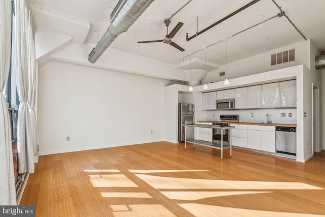 kitchen with white cabinetry, a high ceiling, ceiling fan, light hardwood / wood-style floors, and stainless steel appliances