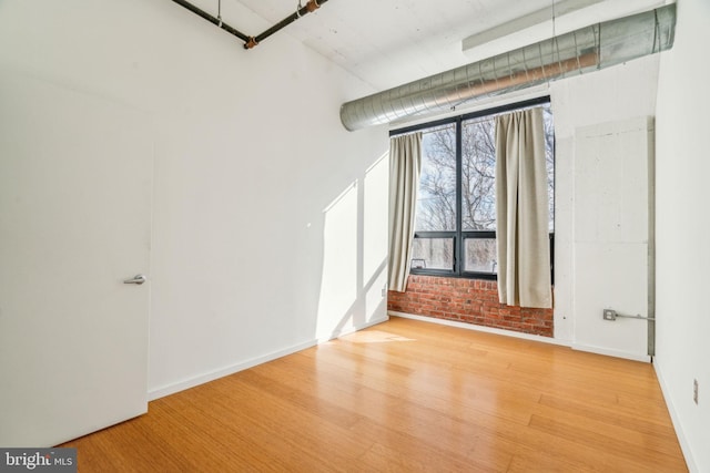 spare room featuring brick wall and wood-type flooring