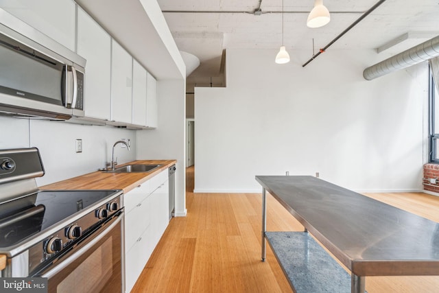 kitchen featuring sink, hanging light fixtures, stainless steel appliances, white cabinets, and light wood-type flooring