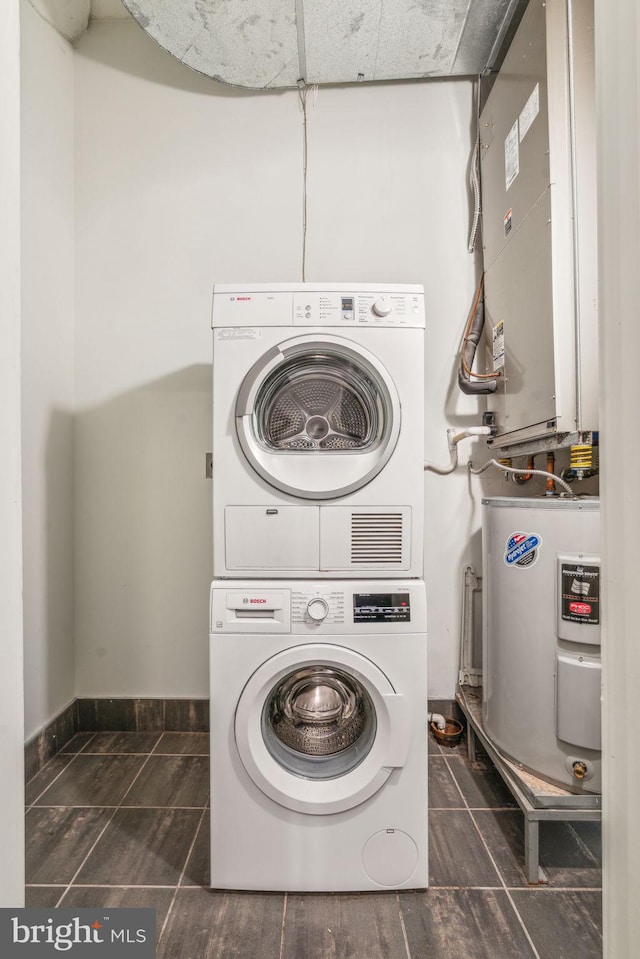 clothes washing area featuring stacked washer and clothes dryer, water heater, and dark tile patterned floors