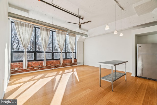 interior space with wood-type flooring, rail lighting, ceiling fan, and brick wall