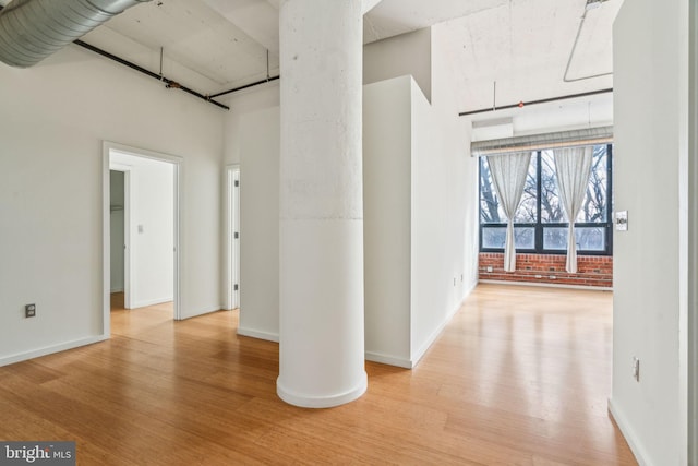 corridor featuring brick wall, a high ceiling, and light wood-type flooring