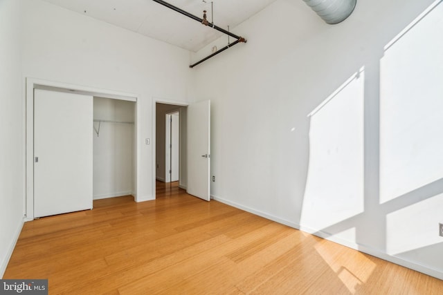 unfurnished bedroom featuring a high ceiling, wood-type flooring, and a closet