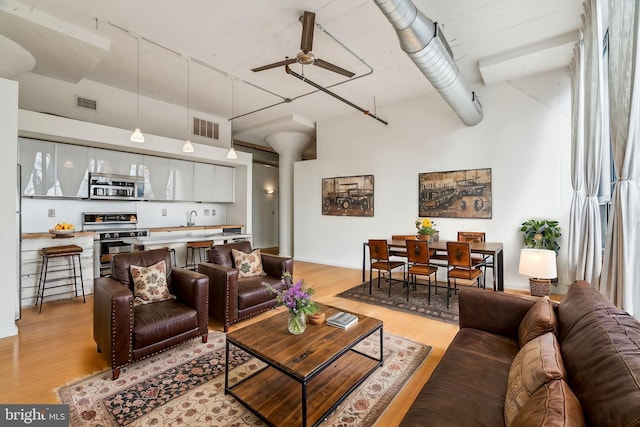 living room featuring ceiling fan, a towering ceiling, sink, and light hardwood / wood-style flooring