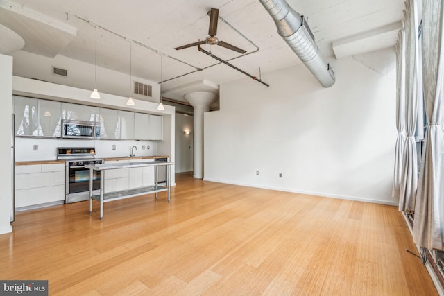 kitchen featuring ceiling fan, a towering ceiling, stainless steel appliances, white cabinets, and light wood-type flooring