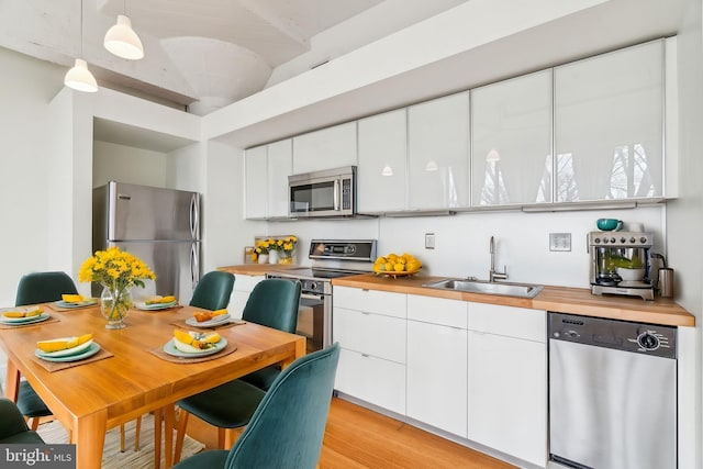 kitchen with pendant lighting, white cabinetry, sink, stainless steel appliances, and light hardwood / wood-style flooring