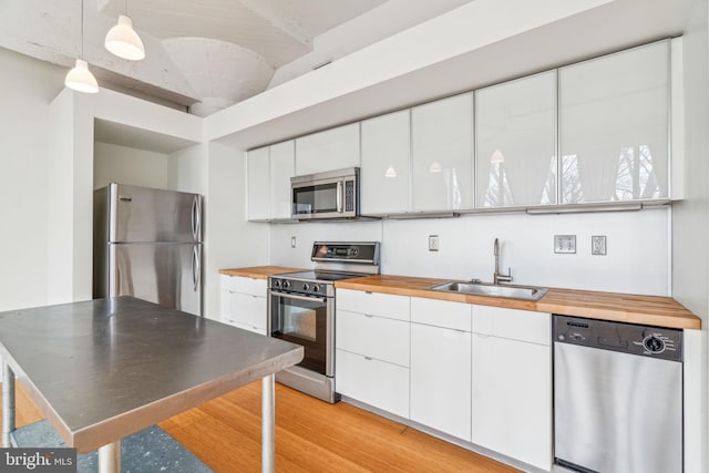 kitchen with sink, decorative light fixtures, appliances with stainless steel finishes, light hardwood / wood-style floors, and white cabinets