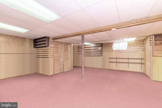 basement with carpet flooring, a paneled ceiling, and wooden walls