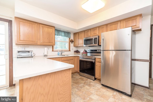 kitchen with appliances with stainless steel finishes, sink, decorative backsplash, kitchen peninsula, and light brown cabinets