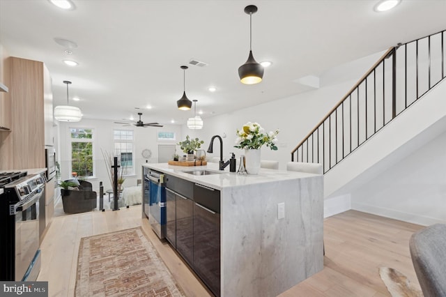 kitchen featuring an island with sink, decorative light fixtures, sink, stainless steel dishwasher, and gas range oven