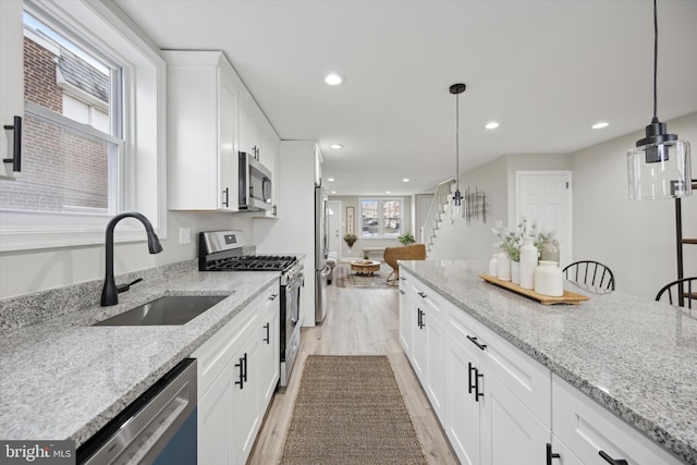 kitchen with white cabinetry, hanging light fixtures, sink, and appliances with stainless steel finishes