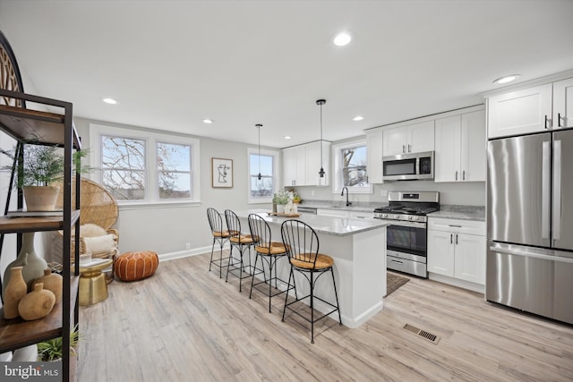 kitchen featuring white cabinetry, hanging light fixtures, appliances with stainless steel finishes, a kitchen island, and light stone countertops