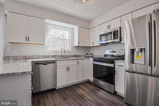 kitchen featuring dark wood finished floors, light stone counters, white cabinets, stainless steel appliances, and a sink