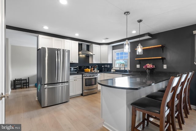 kitchen with dark countertops, wall chimney exhaust hood, a peninsula, and appliances with stainless steel finishes