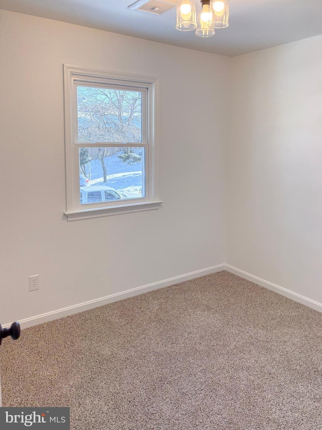 carpeted spare room with an inviting chandelier