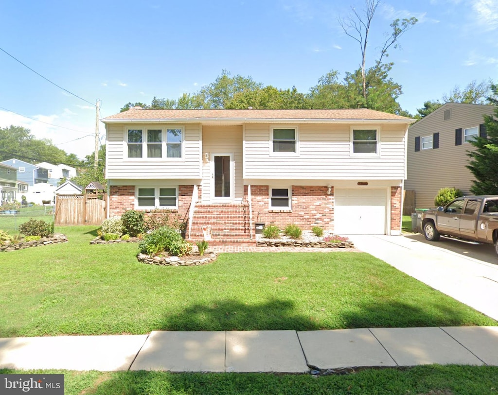 raised ranch with fence, an attached garage, a front lawn, concrete driveway, and brick siding