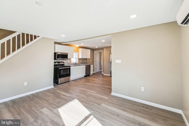 kitchen with light hardwood / wood-style flooring, stainless steel appliances, an AC wall unit, white cabinets, and sink