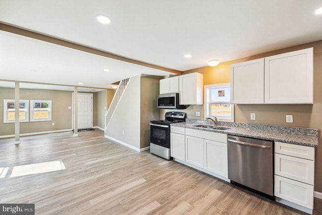 kitchen with white cabinetry, stainless steel appliances, a wealth of natural light, sink, and light stone counters