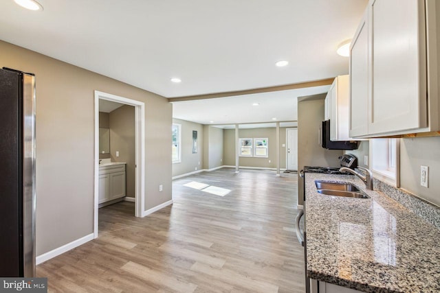 kitchen with sink, stone countertops, light wood-type flooring, stainless steel appliances, and white cabinets