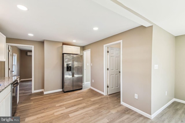 kitchen with light wood-type flooring, appliances with stainless steel finishes, white cabinetry, and light stone counters