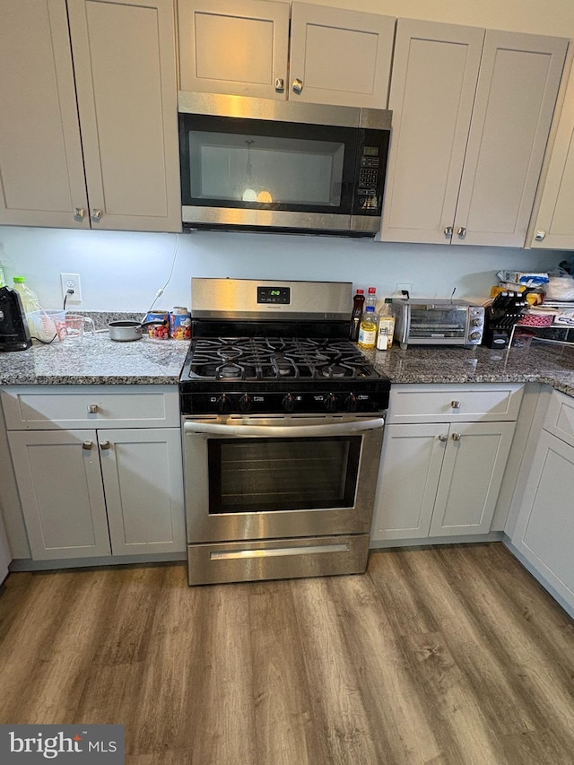 kitchen with stone counters, appliances with stainless steel finishes, gray cabinetry, and light hardwood / wood-style flooring