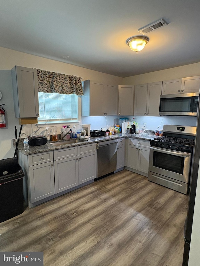 kitchen with sink, dark stone countertops, gray cabinetry, stainless steel appliances, and dark wood-type flooring