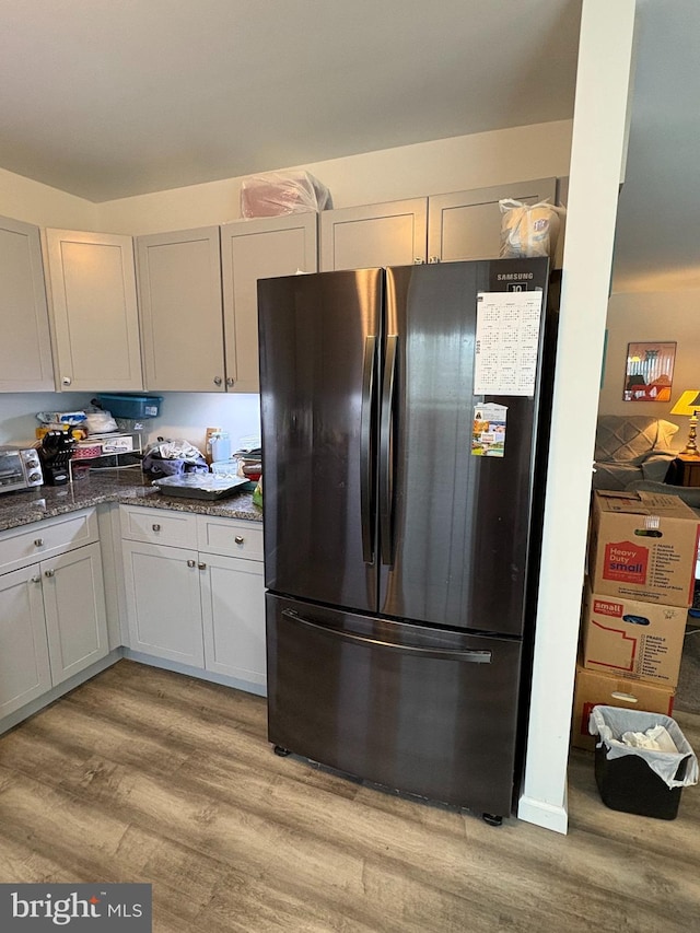 kitchen with white cabinetry, dark stone counters, refrigerator, and light hardwood / wood-style floors