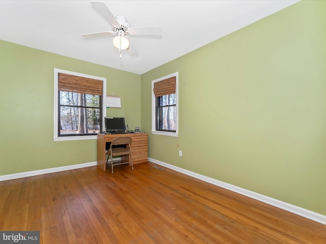 unfurnished office with ceiling fan, a healthy amount of sunlight, and wood-type flooring