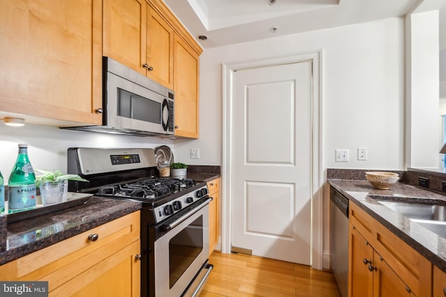 kitchen with appliances with stainless steel finishes, light hardwood / wood-style flooring, sink, and dark stone counters