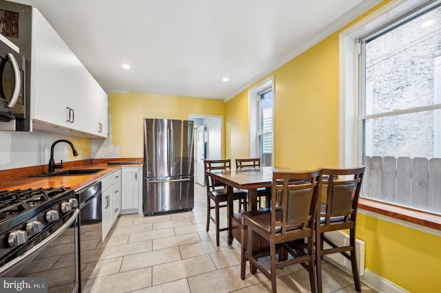 kitchen with sink, white cabinets, ornamental molding, light tile patterned floors, and stainless steel appliances