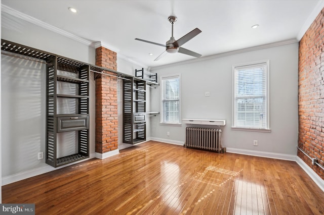 unfurnished bedroom with crown molding, ceiling fan, hardwood / wood-style floors, radiator heating unit, and brick wall