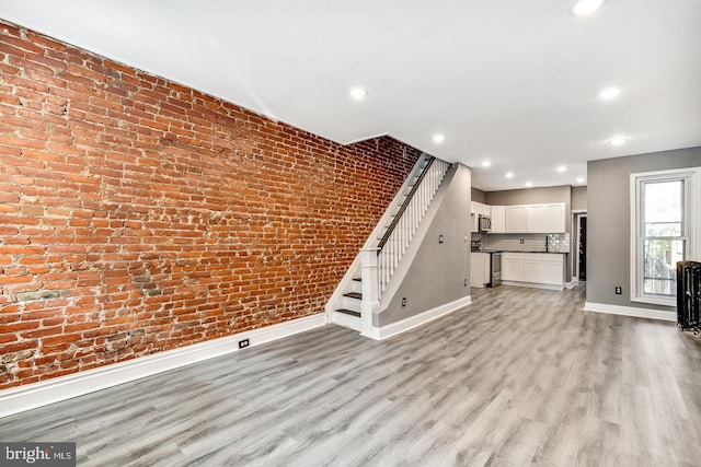 unfurnished living room featuring brick wall and light wood-type flooring