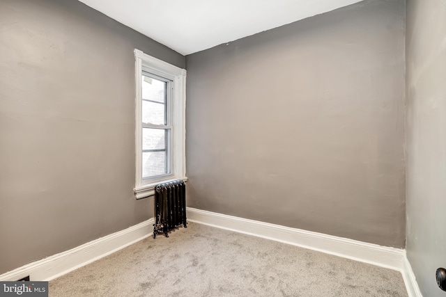 spare room featuring light carpet and radiator