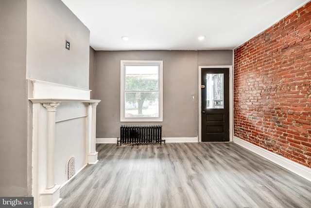 foyer entrance with brick wall, radiator, and light hardwood / wood-style flooring