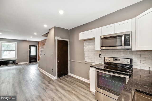 kitchen with light hardwood / wood-style flooring, white cabinetry, radiator heating unit, stainless steel appliances, and tasteful backsplash