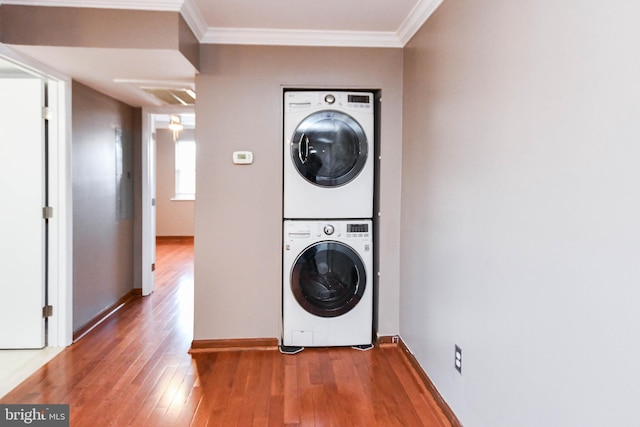 clothes washing area featuring stacked washer / drying machine, ornamental molding, and hardwood / wood-style floors