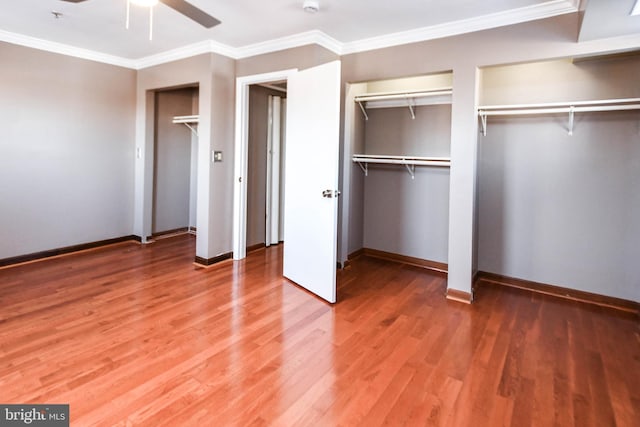 unfurnished bedroom featuring ceiling fan, crown molding, wood-type flooring, and multiple closets