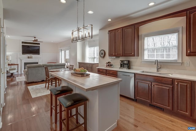 kitchen with sink, a center island, stainless steel dishwasher, a kitchen breakfast bar, and light hardwood / wood-style floors