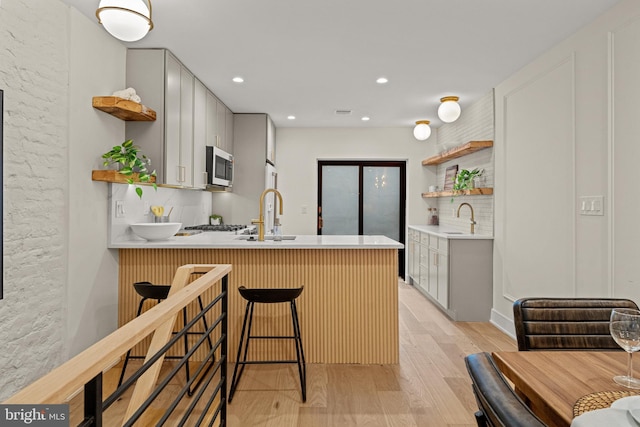 kitchen featuring sink, backsplash, a kitchen bar, light hardwood / wood-style floors, and kitchen peninsula