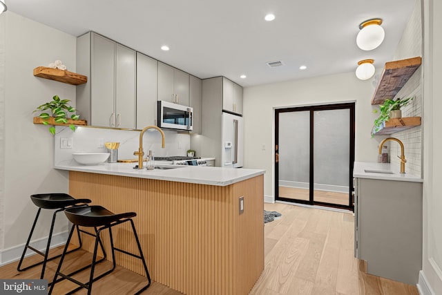 kitchen featuring sink, gray cabinets, a kitchen bar, kitchen peninsula, and light wood-type flooring