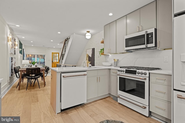 kitchen with sink, light hardwood / wood-style flooring, kitchen peninsula, white appliances, and decorative backsplash